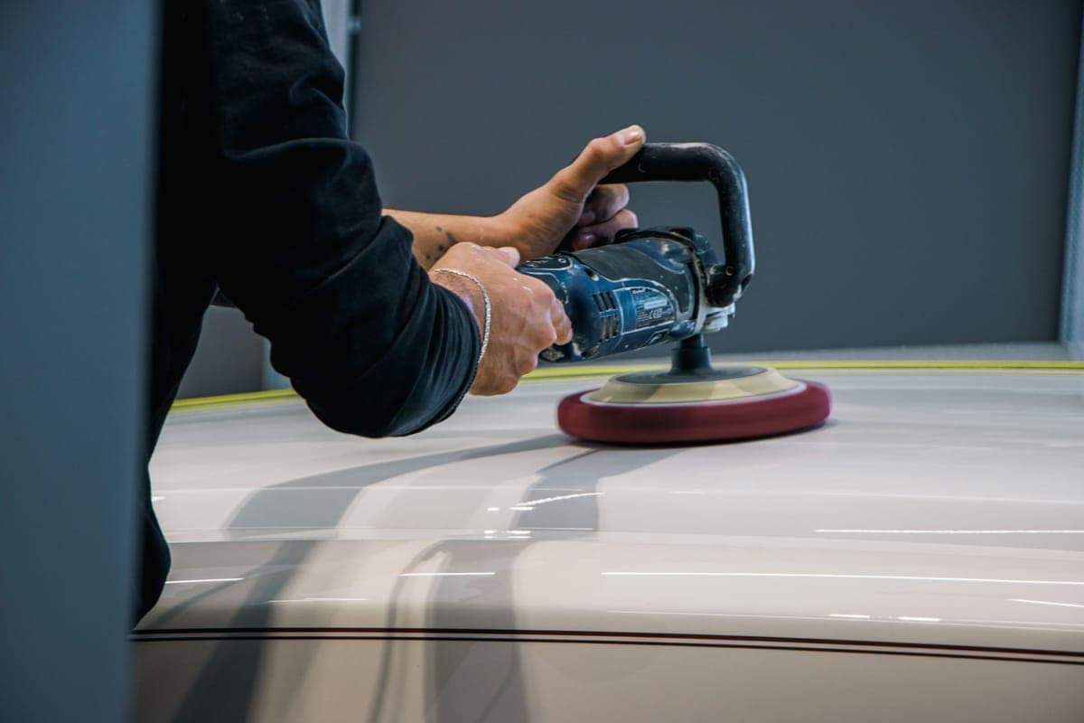 A polisher with a red-backed pad working across a white car panel