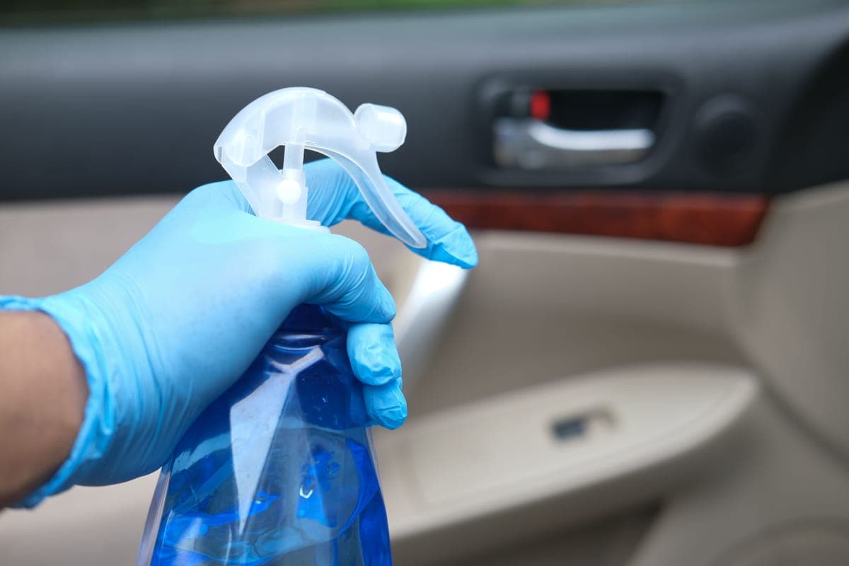 A spray bottle and a folded microfiber towel on a car's door sill