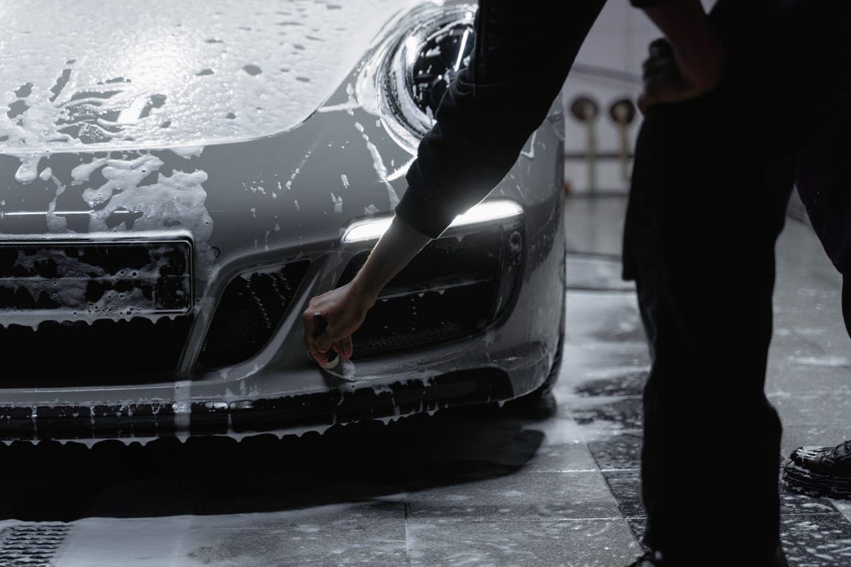 The front bumper and headlight of a car being sprayed with cleaner