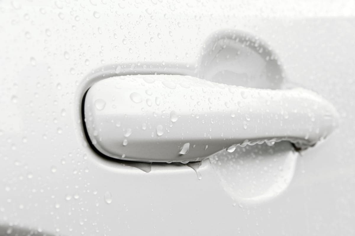 Water being blown off the side mirror and door of a freshly washed car