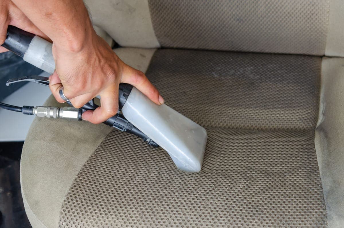 A brush agitating foam on a gray cloth car seat