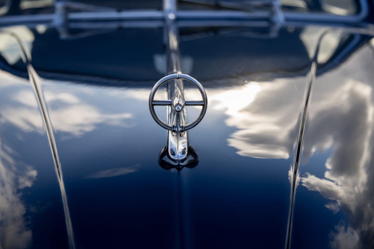 A glossy black car hood reflecting a bright overcast sky
