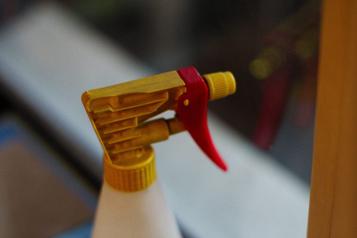 A spray bottle misting a light gray car panel with a folded towel beside it