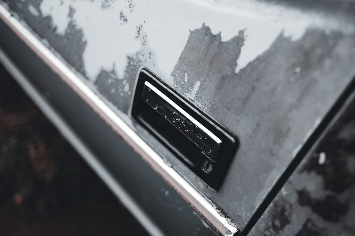 A weathered car door with chrome trim and a dull, patchy finish