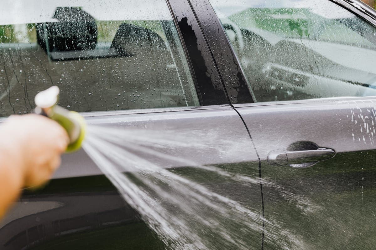 A clean car being rinsed with a hose in a driveway