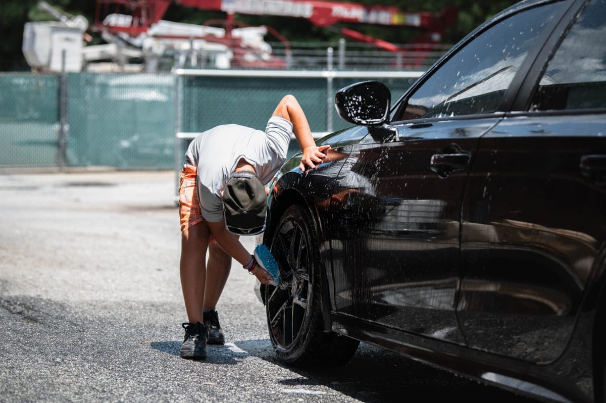 Washing the wheel of a black car with a wash mitt