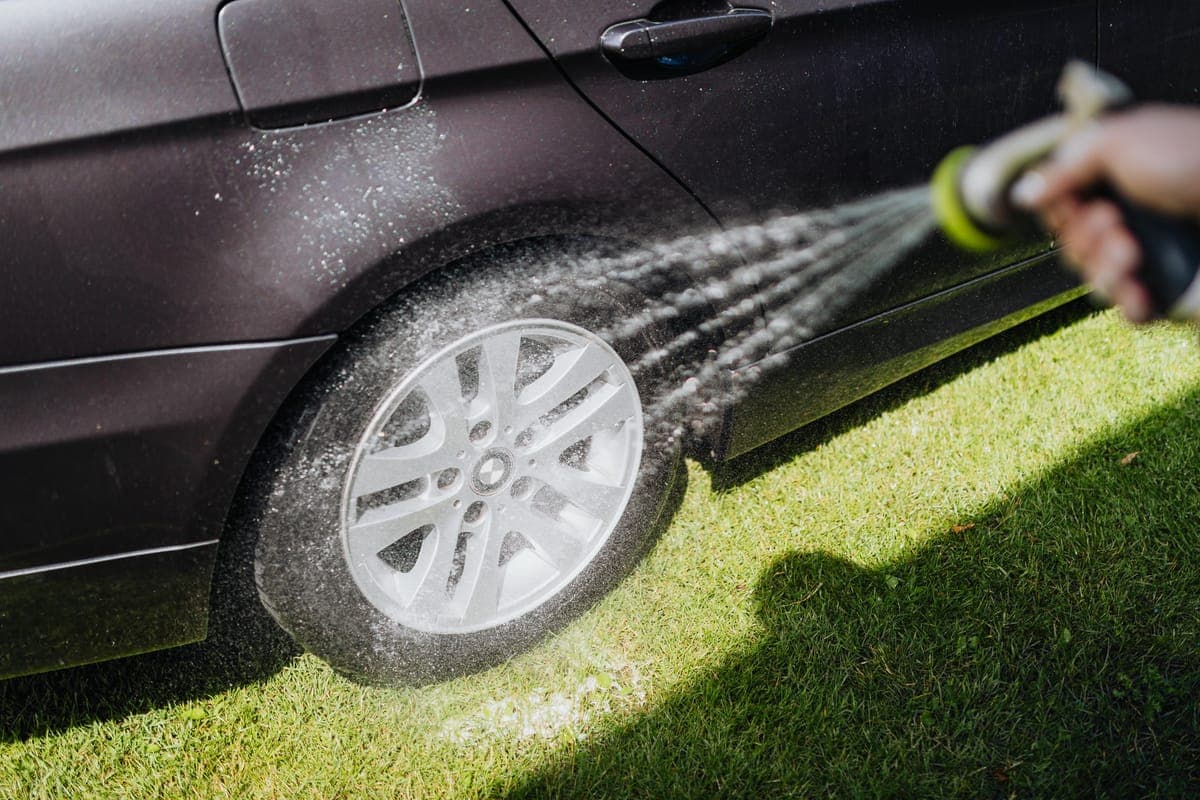 A foam gun attached to a garden hose beside a partially foamed car