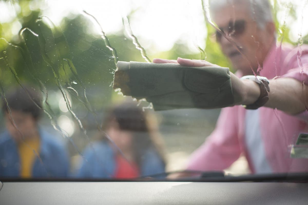 A tinted car window being wiped clean with a folded microfiber towel