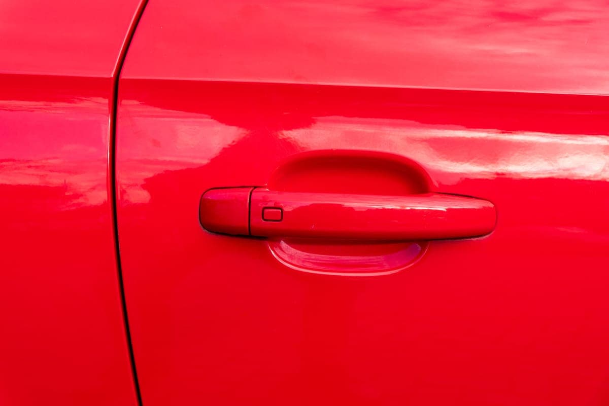 A close-up of a glossy red car door and handle