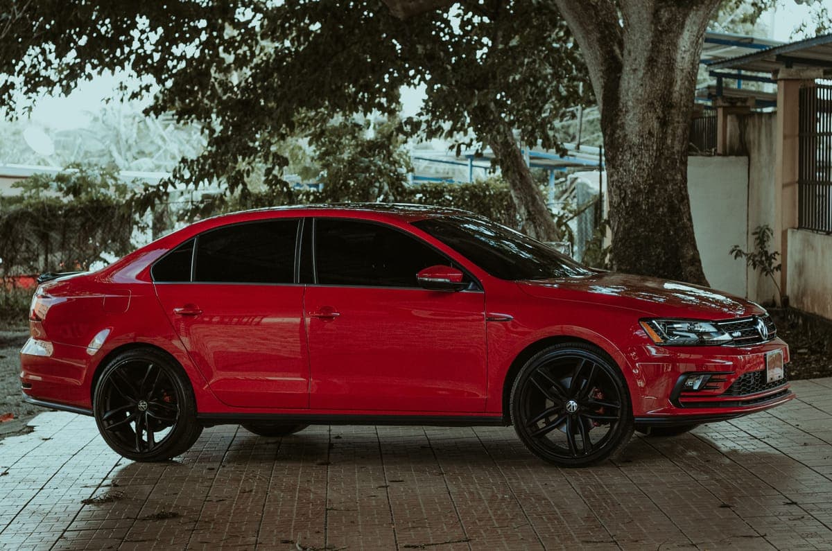A clean red sedan parked under a tree