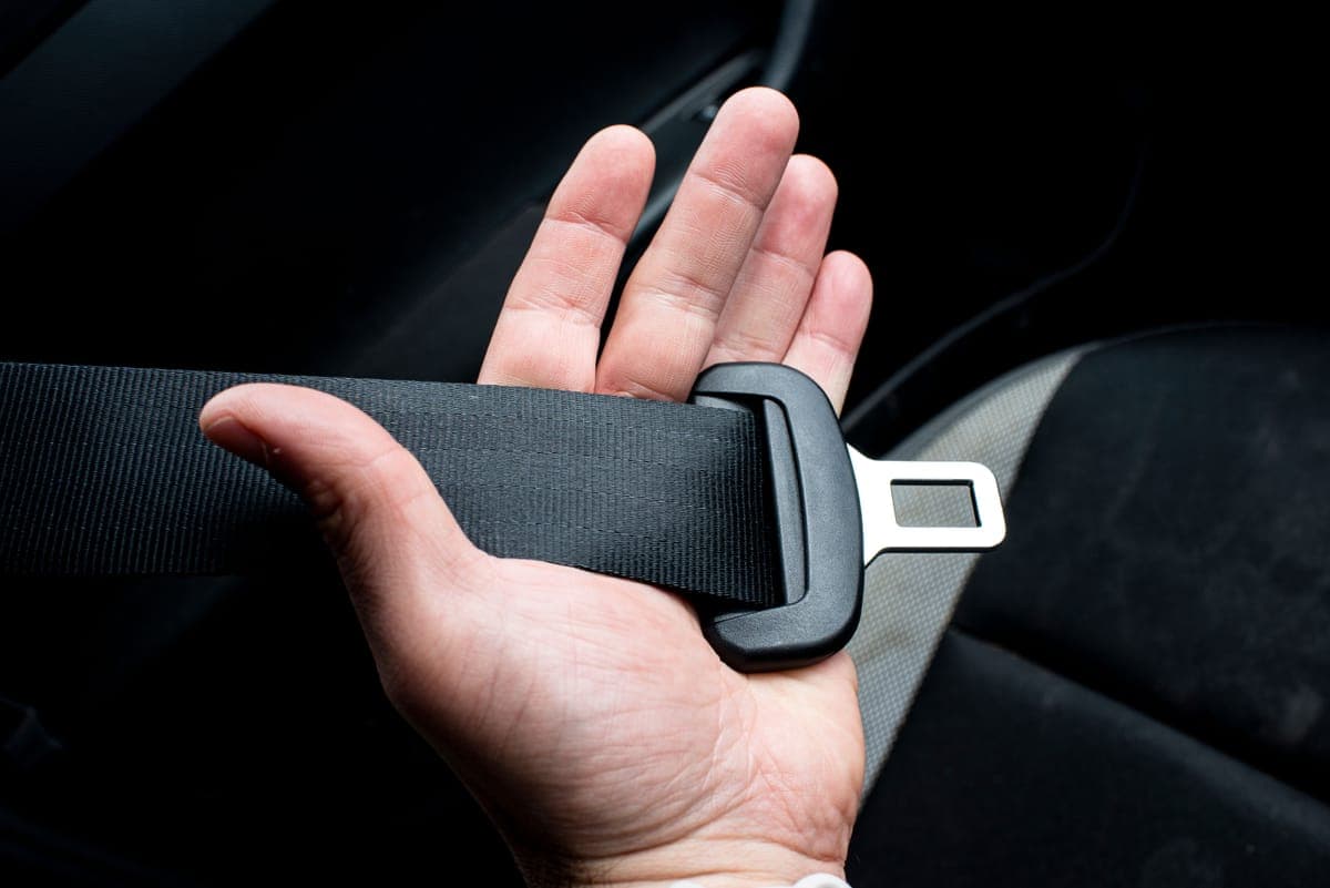 A hand holding a seat belt tongue and webbing inside a car
