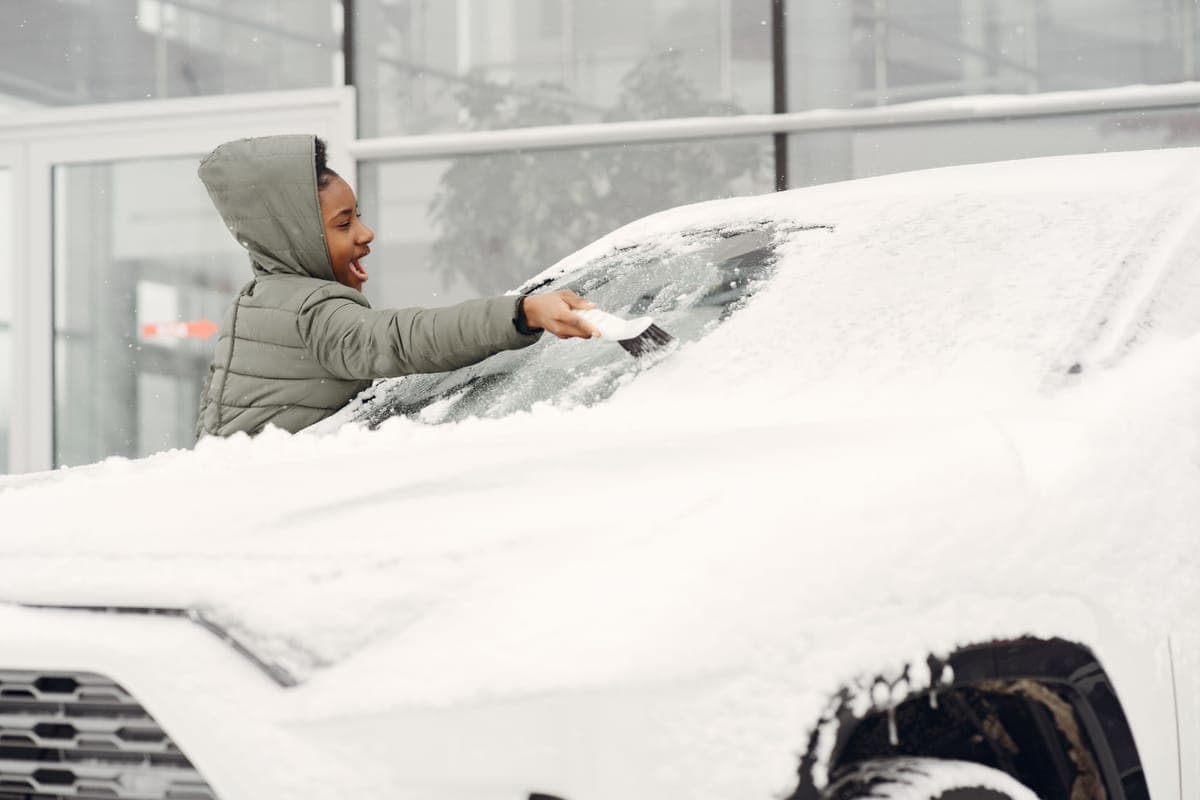 Snow being cleared from a car windshield with a brush