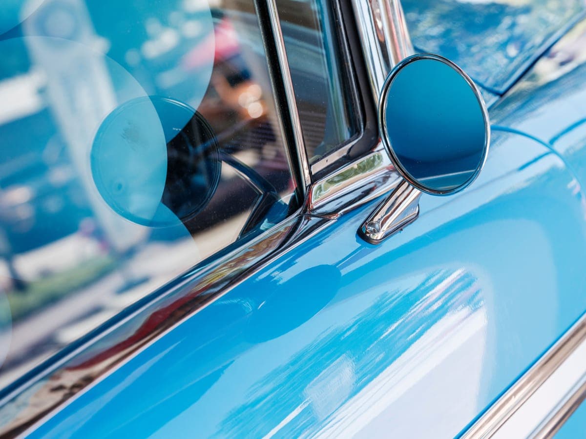 Reflections across the flank and chrome mirror of a light blue classic car