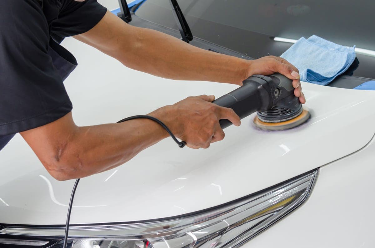 A polisher working across a taped-off car panel under bright light