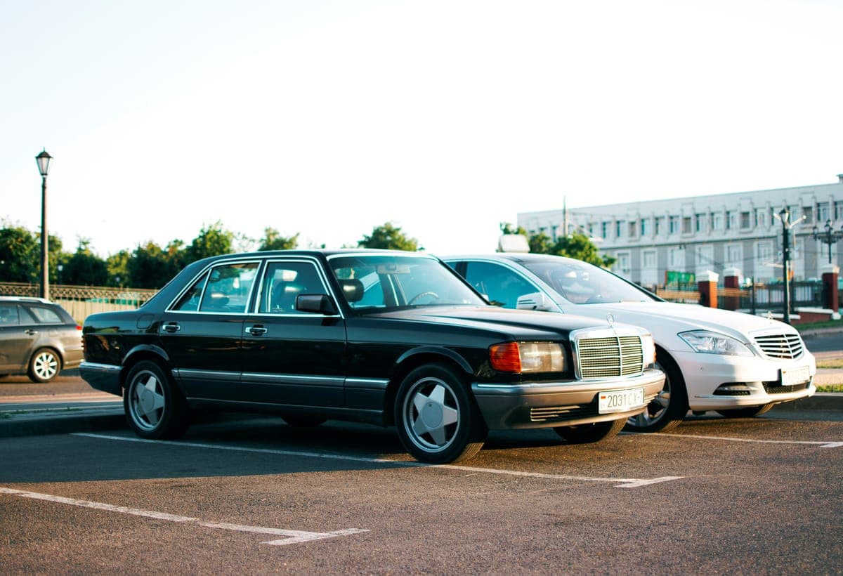 Two sedans parked in an open lot under a bright sky