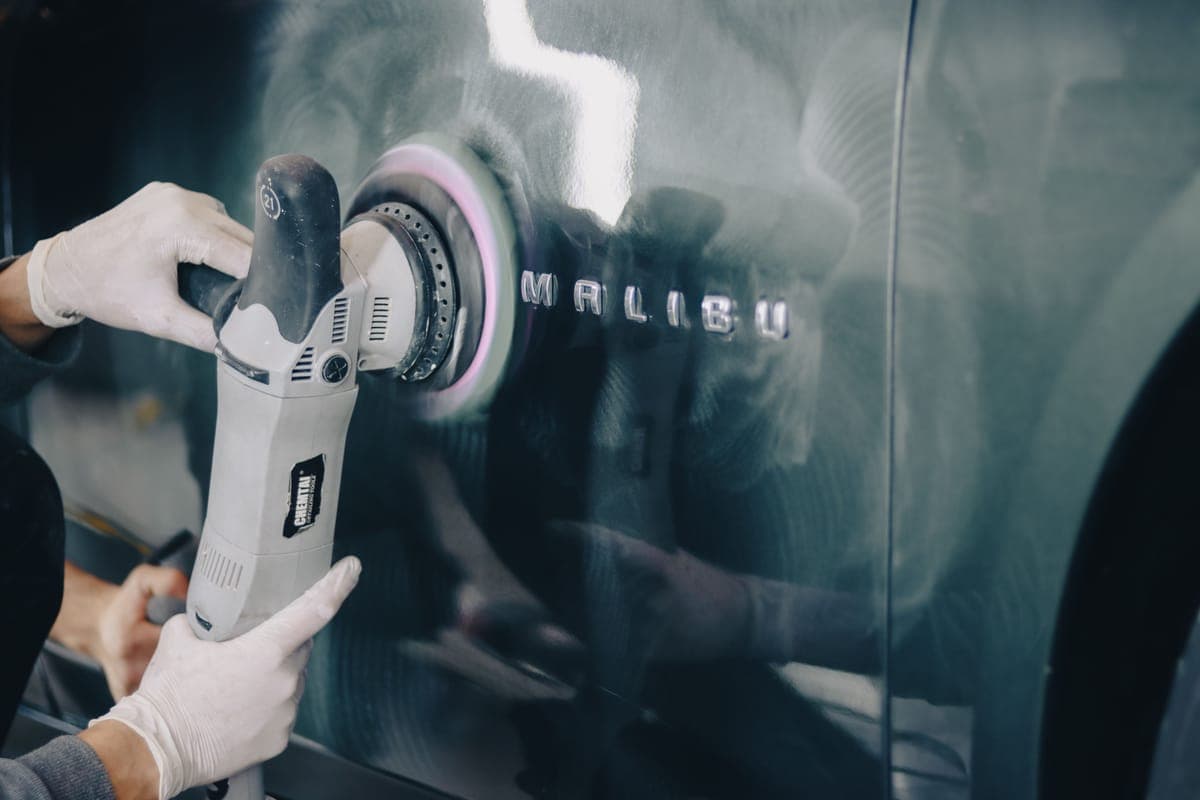 A dual action polisher working across a dark car panel