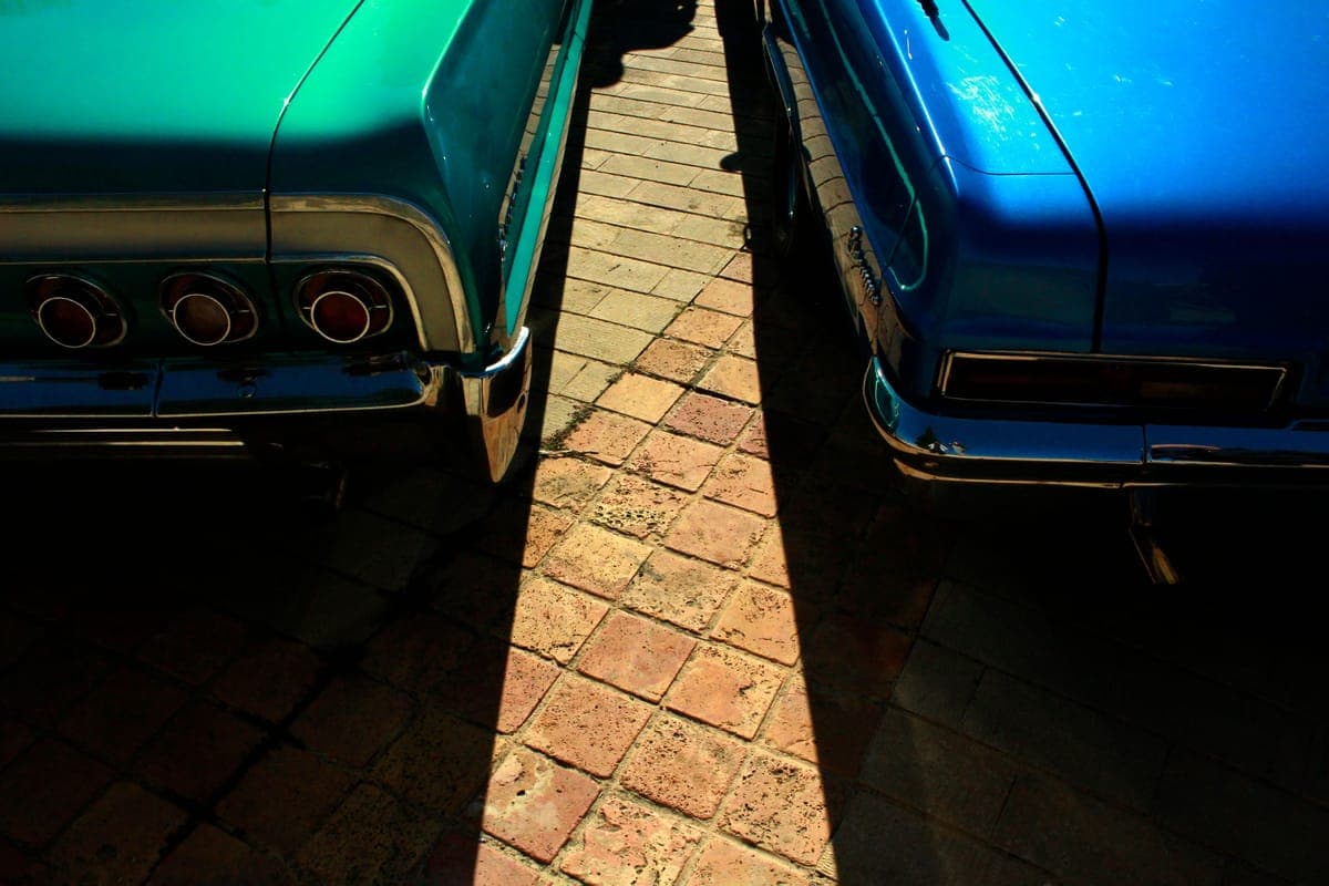 Sunlight and shade falling across the rear ends of two classic cars