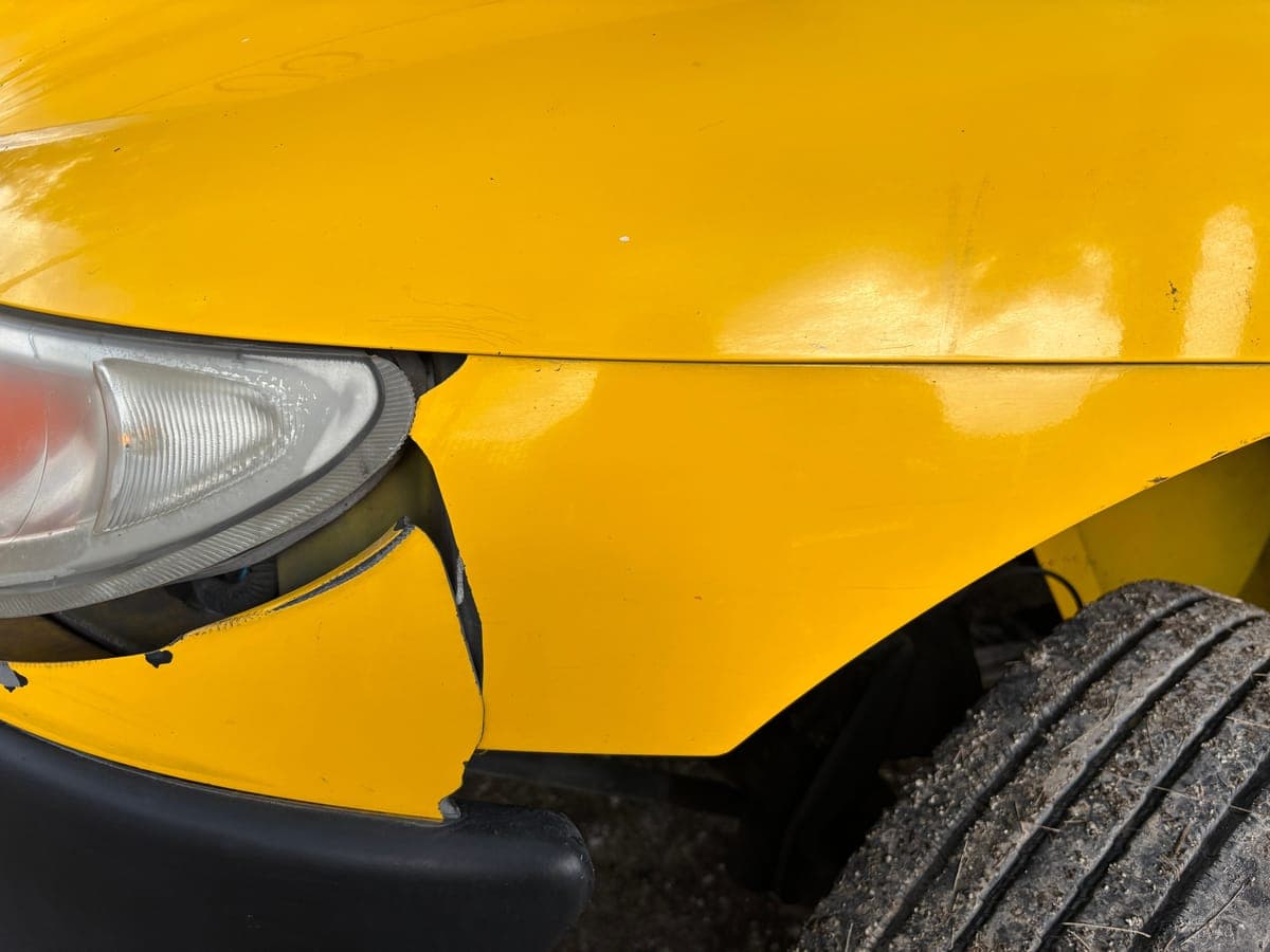 A scraped and split front bumper corner on a yellow car