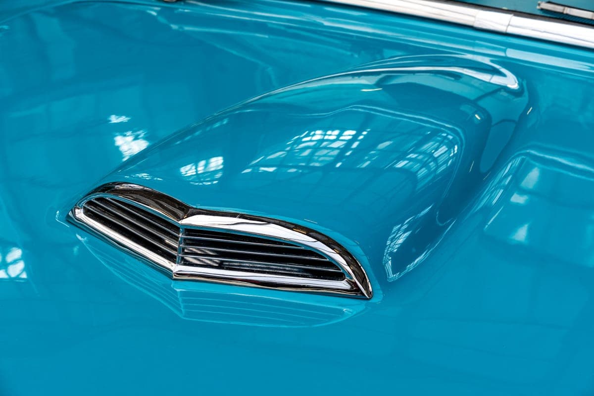 Reflections across the glossy turquoise hood of a classic car