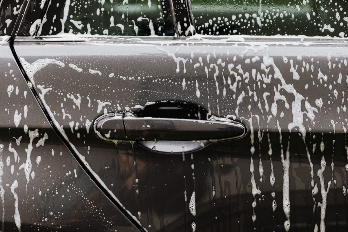 A black car panel covered in soap suds during a hand wash