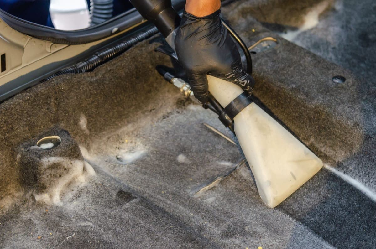 A car's carpeted floor being cleaned with an extraction hand tool