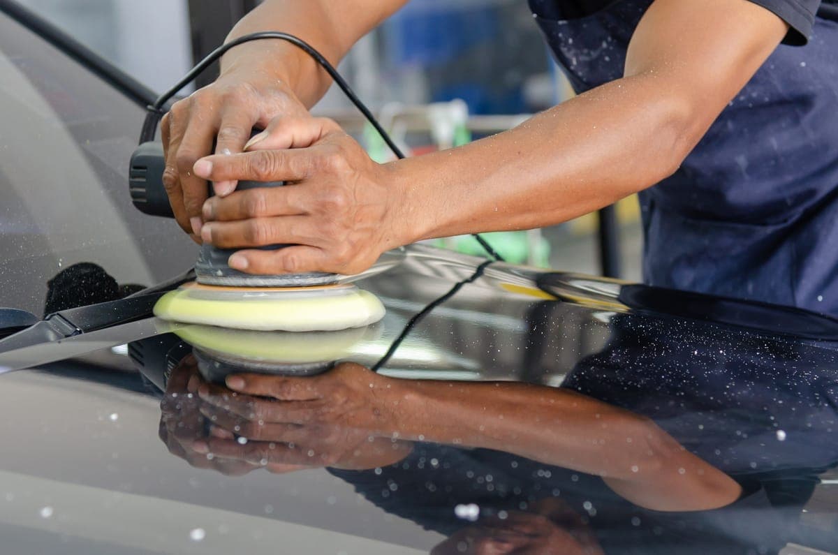 A dual action polisher resting on the hood of a car mid-correction
