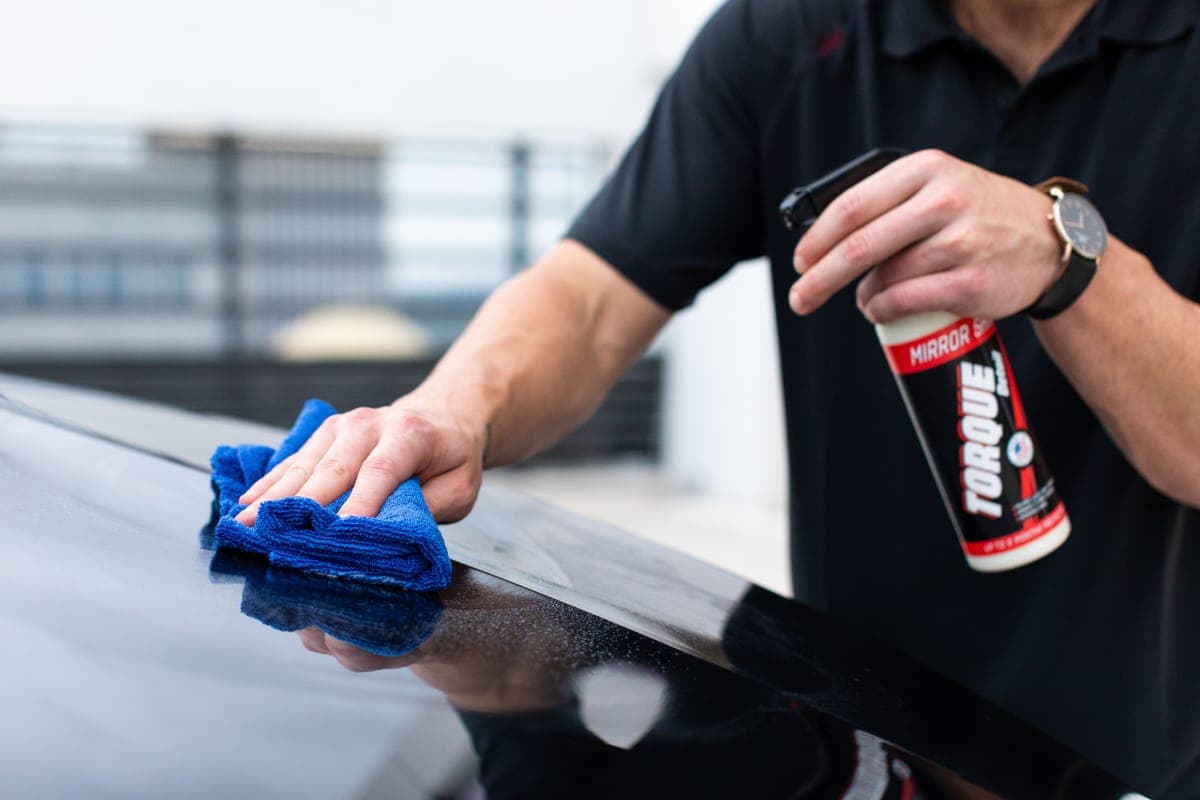 A blue microfiber towel being drawn across a wet dark hood