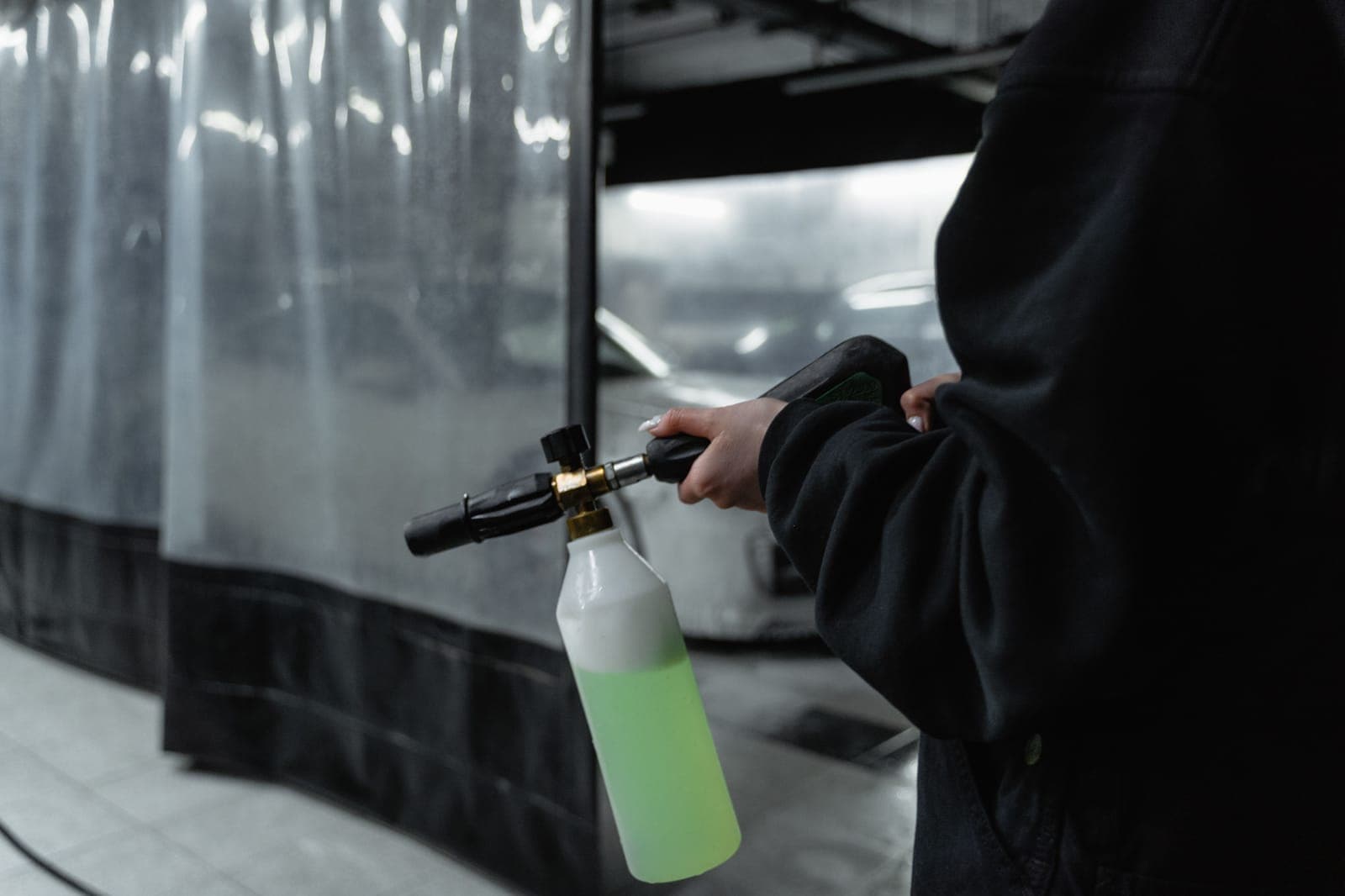 A brass-bodied foam cannon with a soap-filled bottle attached to a pressure washer gun, held in a wash bay