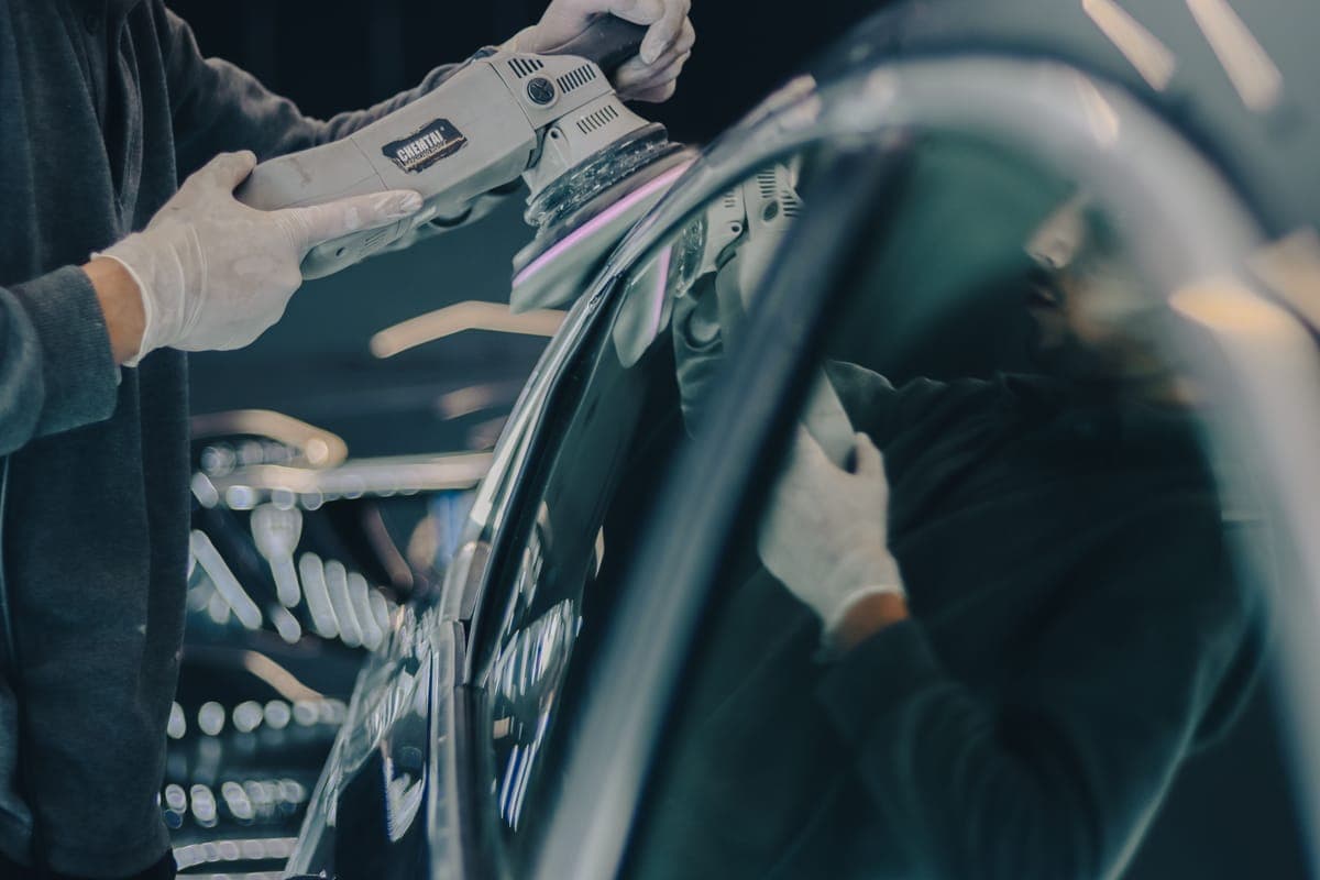 Gloved hands running a polisher along the roofline of a car