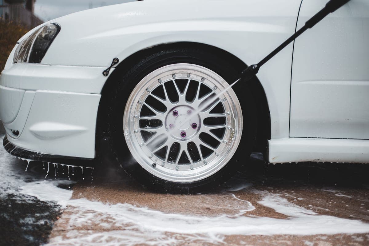 A pressure washer jet rinsing a wheel with foam running off the car