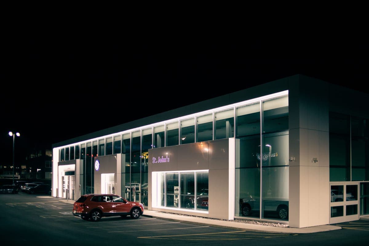 A lit car dealership building at night with a red SUV parked outside