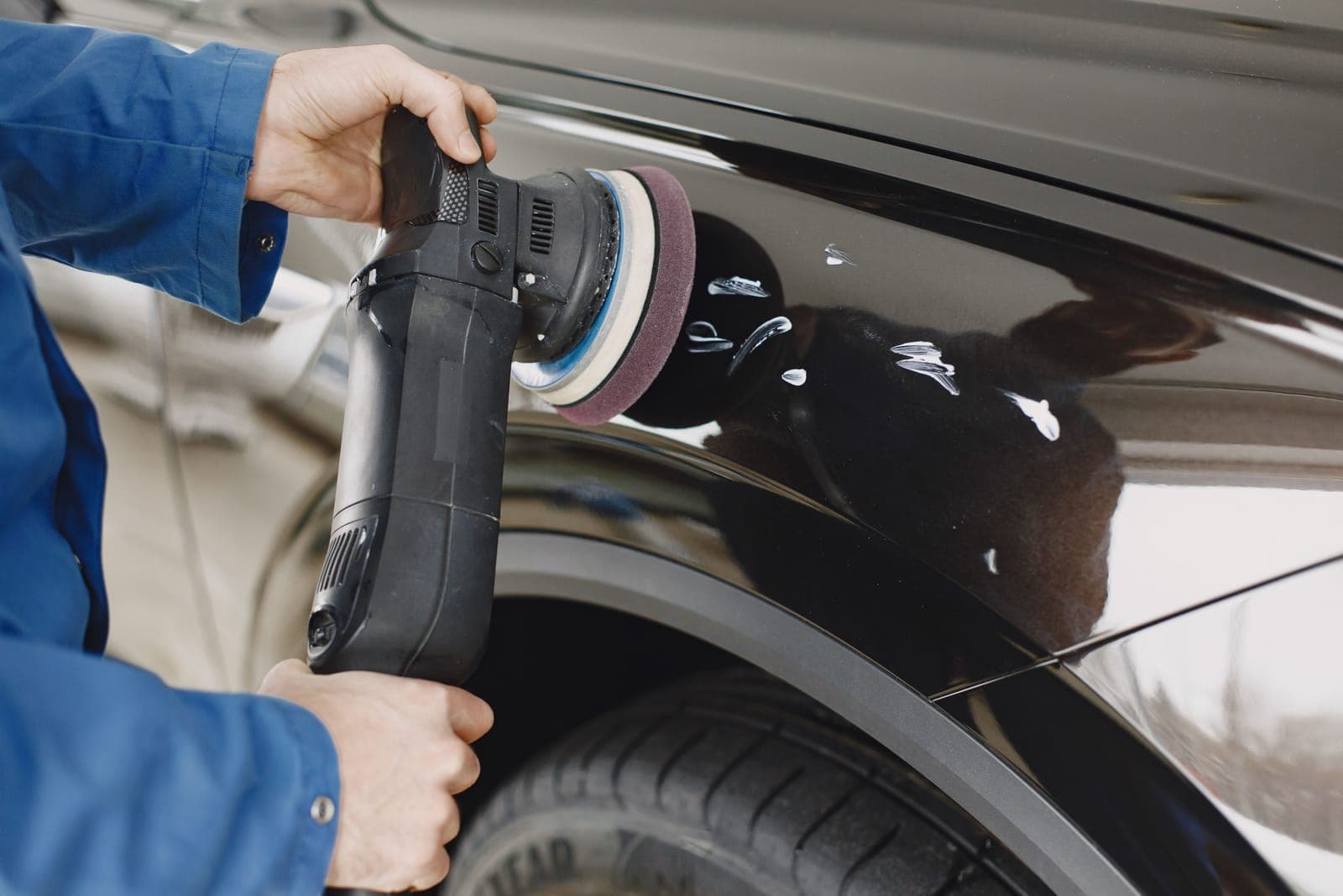 A dual action polisher with a foam pad resting on a glossy dark blue car panel
