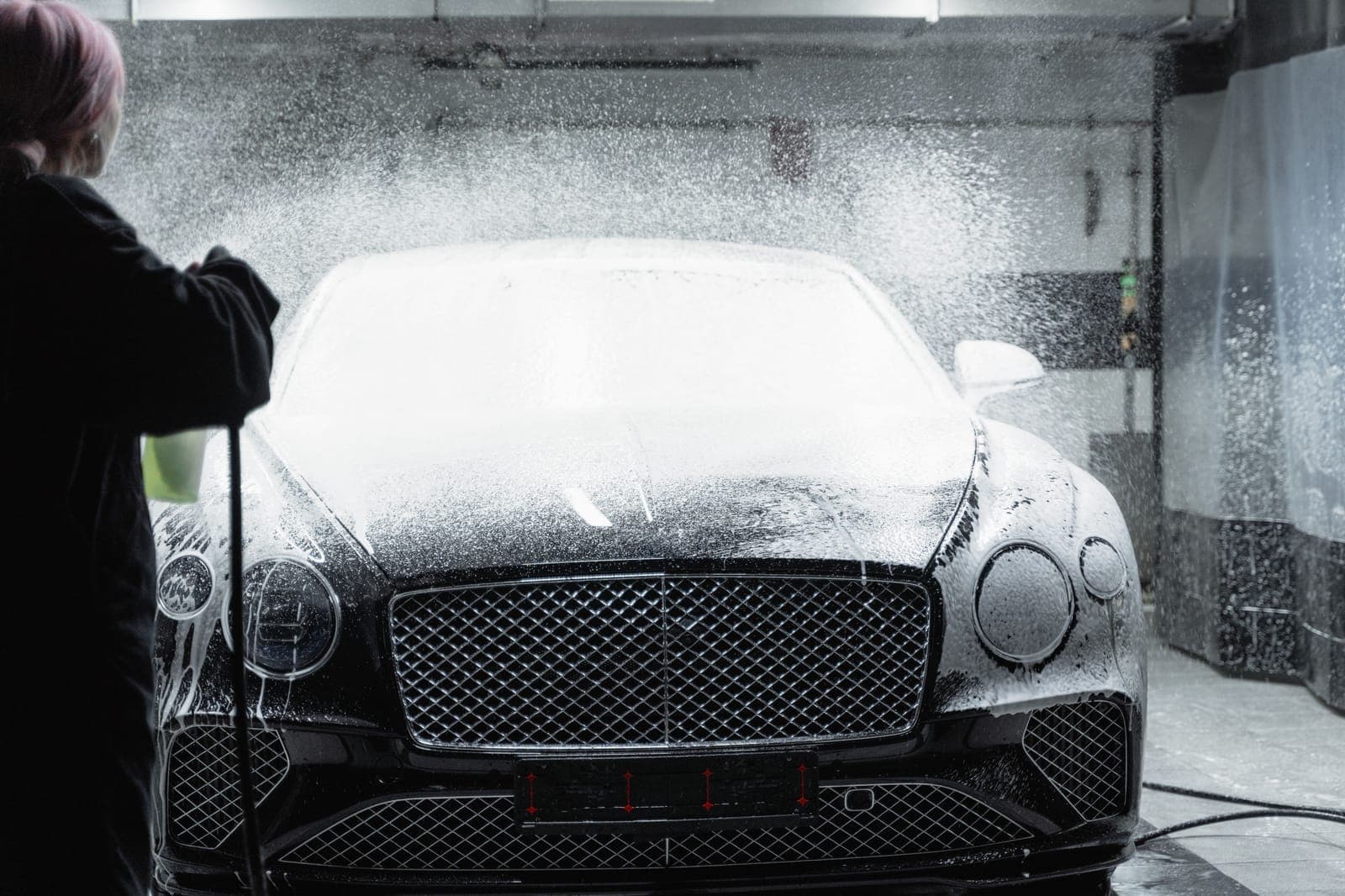 Thick white foam clinging to the hood and fender of a light-colored car in daylight